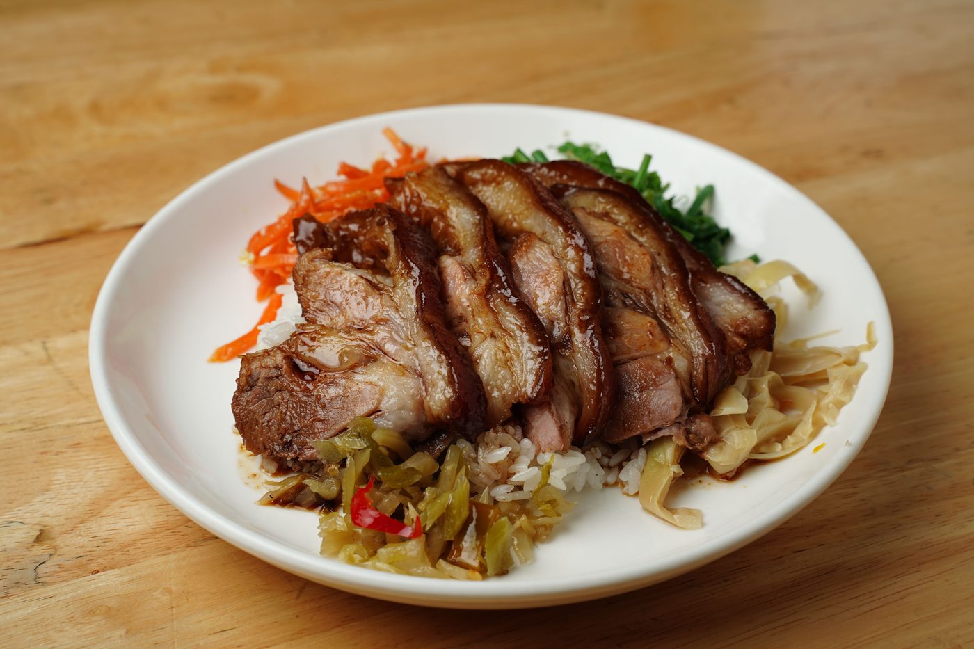 Sliced braised pork knuckle over white rice with pickled greens, carrot and cabbage